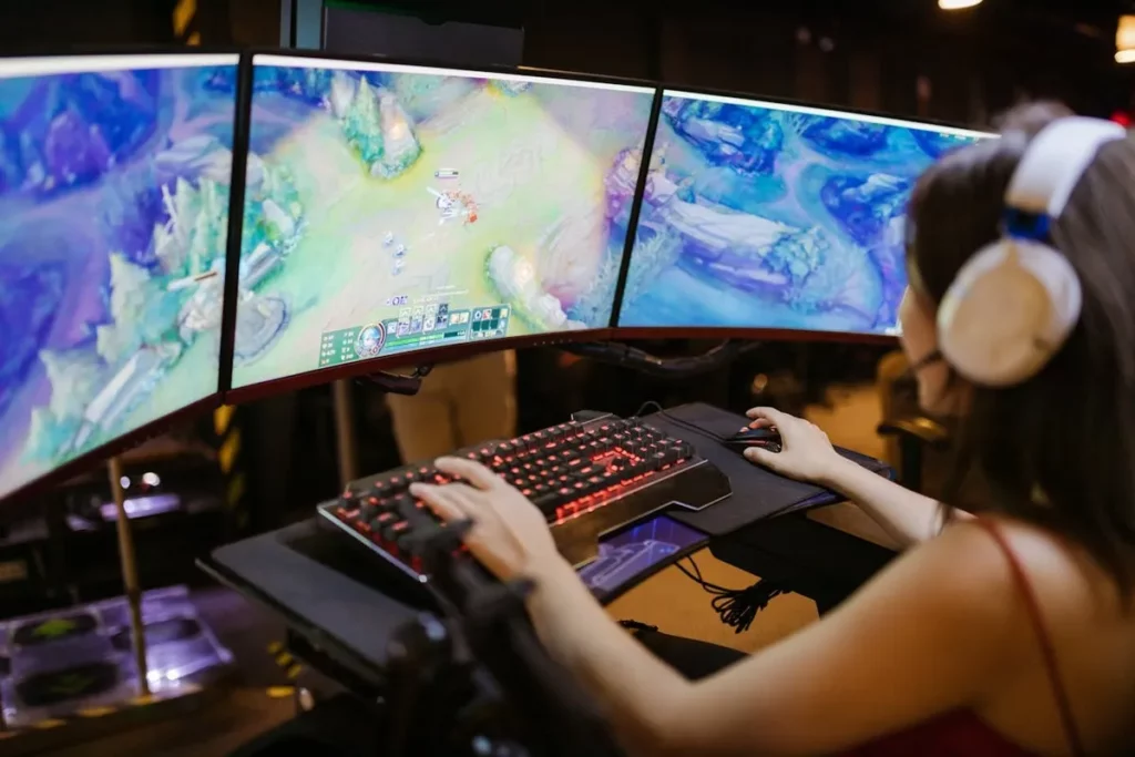 Pessoa jogando em setup gamer com teclado mecânico RGB e três monitores curvos exibindo jogo de estratégia.