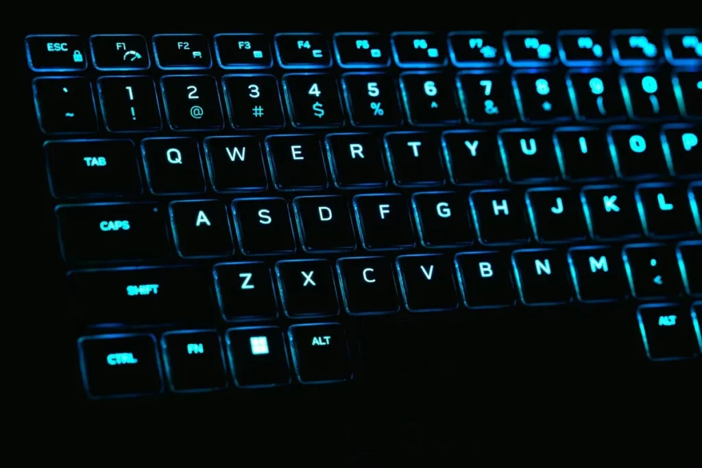 Teclado de notebook com retroiluminação azul e layout QWERTY, fotografado em ambiente escuro.