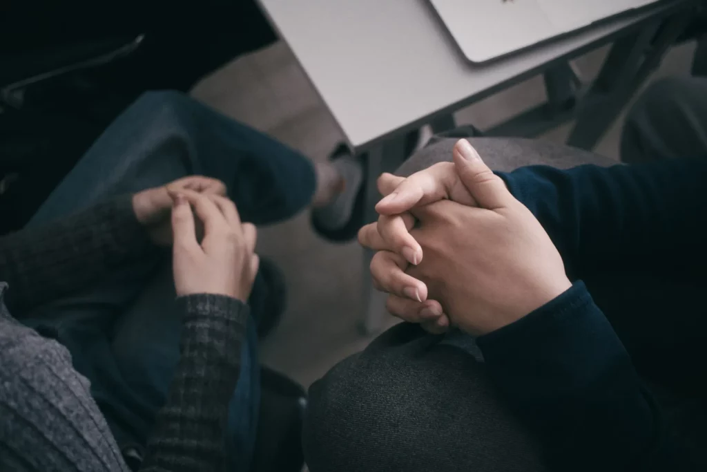 Duas pessoas sentadas com as mãos entrelaçadas em sinal de apoio emocional durante uma conversa.
