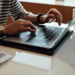 Pessoa digitando em um notebook com uma xícara de café ao lado