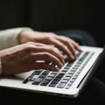 Mãos femininas digitando em um teclado de laptop, representando concentração e produtividade no ambiente de trabalho ou estudos.