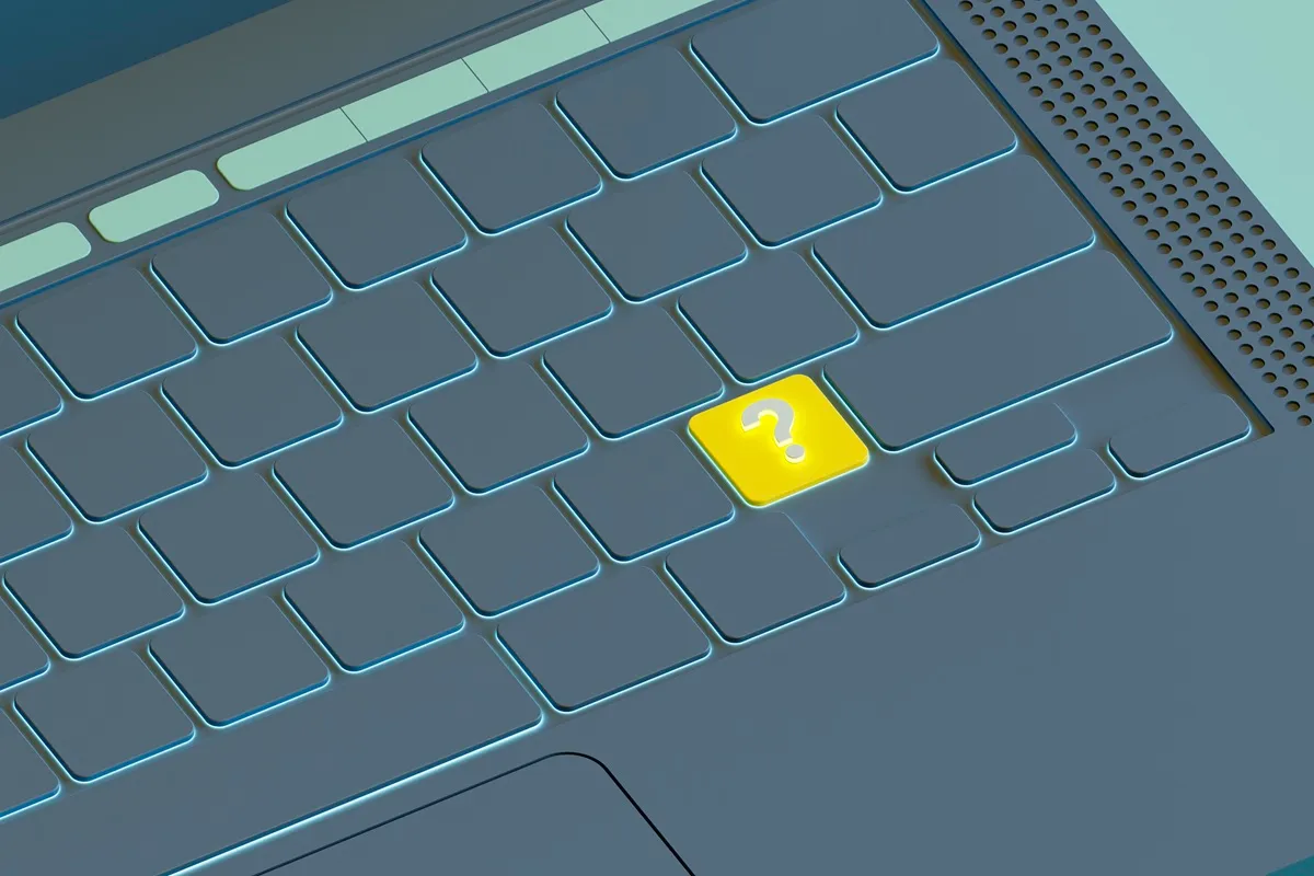 Close-up de teclado de laptop com tecla de pergunta destacada em amarelo brilhante.