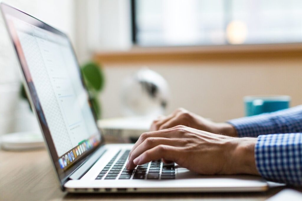 Pessoa digitando em notebook com tela aberta, em ambiente iluminado e profissional