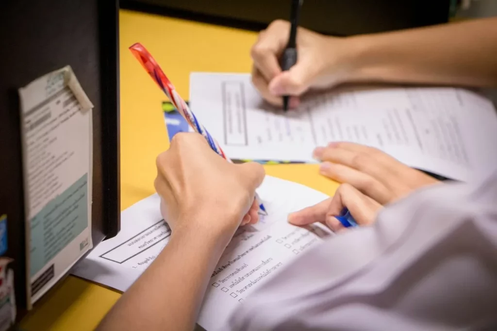 Estudantes preenchendo formulários ou provas com canetas sobre uma mesa amarela