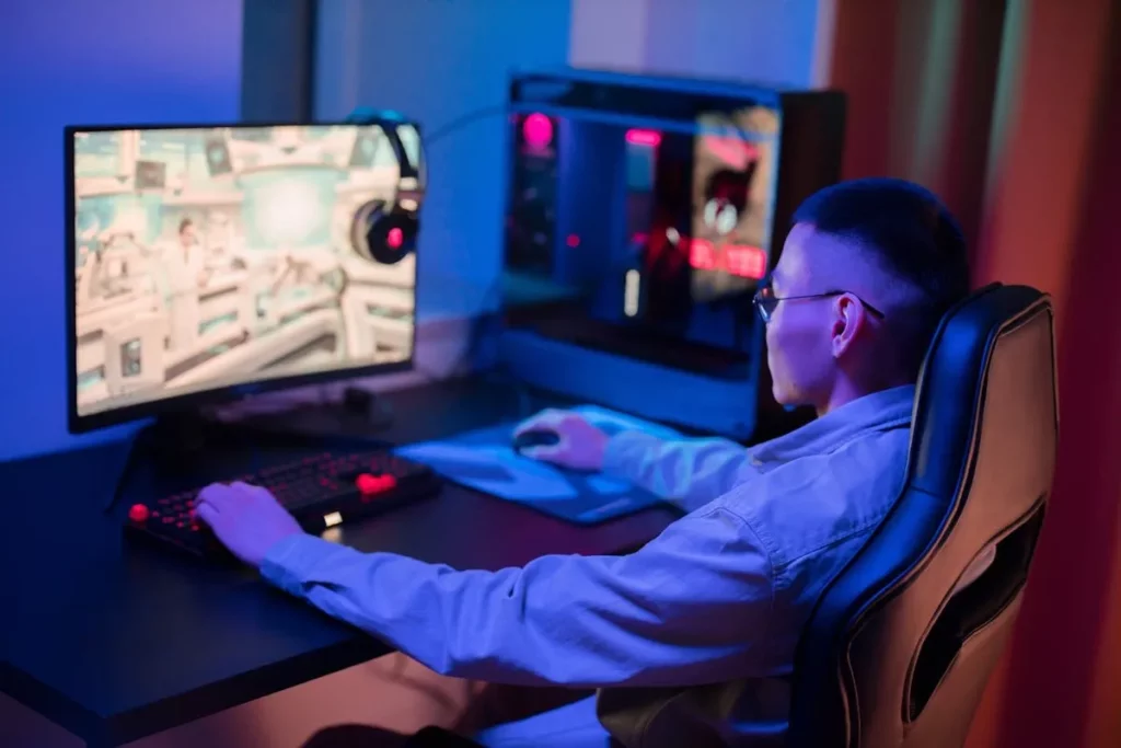 Jovem jogador sentado em uma cadeira gamer preta, usando um computador com iluminação RGB, fones de ouvido e teclado, imerso em um jogo.