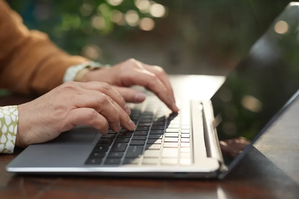 Mãos digitando em um teclado de notebook, aprendendo informática básica. Uso do computador.