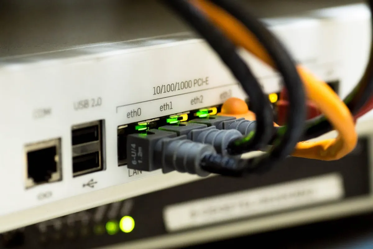 Foco em portas Ethernet e cabos de rede plugados em um roteador ou switch, com luzes indicadoras verdes acesas. A imagem representa a infraestrutura física de rede e a "largura de banda" em ação.