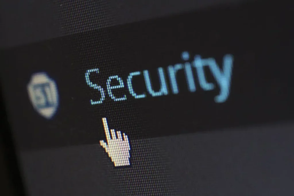 Close-up da tela de um computador mostrando a palavra "Security" em azul e um ícone de escudo, com um cursor de mouse em formato de mão apontando para ela, simbolizando a segurança digital.