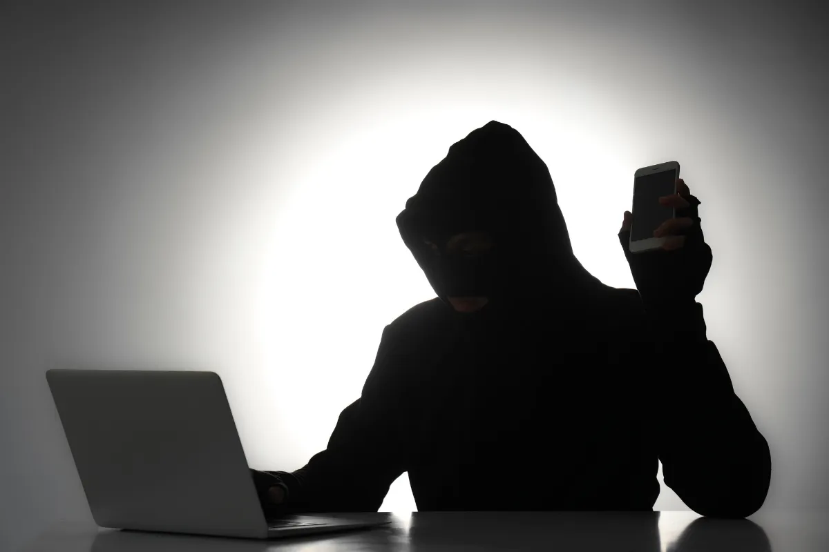 Pessoa de capuz, usando laptop e segurando celular