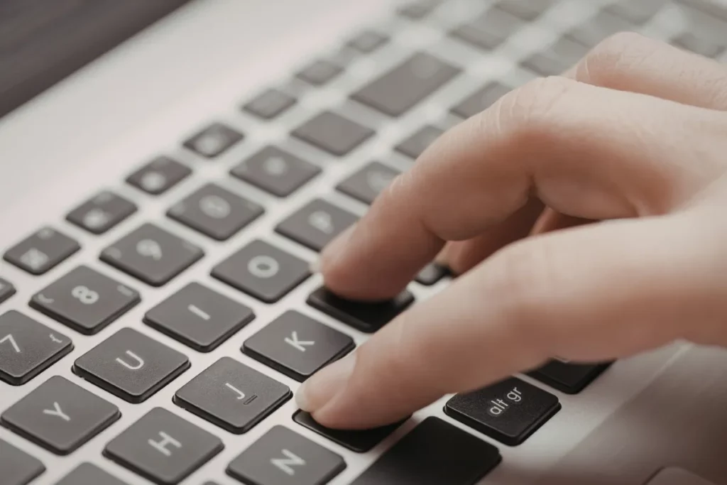 Close de dedos pressionando teclas de um teclado de notebook durante a digitação.
