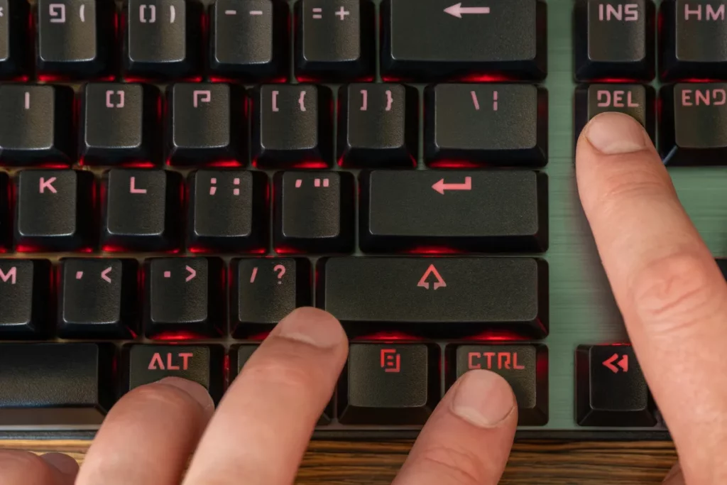 mãos pressionando teclas Alt, Ctrl e Delete em teclado iluminado durante uso do computador