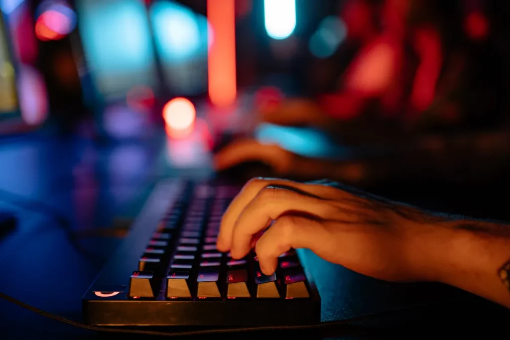 mãos digitando em teclado iluminado com luzes coloridas em ambiente escuro