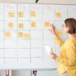 Mulher usando quadro branco e post-its para planejar a semana.